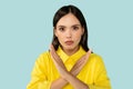 Determined serious beautiful young brunette woman showing crossed hands at camera, blue studio background