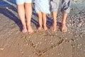 No face family of three standing near drawn heart shape on wet sandy beach in sunlight. Happy family vacation, travel concept. Sel Royalty Free Stock Photo