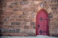 Old red church door off center in brown stone exterior wall with antique hinges Royalty Free Stock Photo