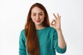 No problem, very well. Smiling young woman with red long hair, look satisfied, make okay zero sign, approve good thing