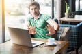 No, stop, please don`t touch me! Young scared businessman in green t-shirt sitting with laptop, looking with afraid face and stop