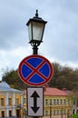 No Stopping sign and plate with black arrow on the post street lamp. Street with blurred buildings in the background Royalty Free Stock Photo