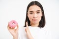 No sweets. Serious young woman on diet, showing stop gesture and glazed doughnut, disapprove junk food, white background Royalty Free Stock Photo