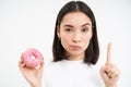 No sweets. Serious young woman on diet, showing stop gesture and glazed doughnut, disapprove junk food, white background Royalty Free Stock Photo