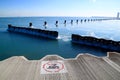 No Swim Sign painted on ledge which runs along Lake Michigan, frozen with icy rocks and view of Chicago Skyline