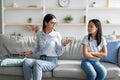 No time for child. Busy asian mom working from home on laptop, sitting on sofa with offended bored daughter nearby Royalty Free Stock Photo