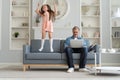 No Time For Child. Grey-haired dad busy with laptop, working online at home, sad bored offended daughter jumping near by Royalty Free Stock Photo