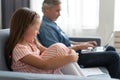 No Time For Child. Grey-haired dad busy with laptop, working online at home, sad bored offended daughter sitting near by Royalty Free Stock Photo