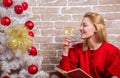 Noel and joy. Girl in red dress relaxing with glass of champagne near christmas tree. Woman happy drink alcohol near