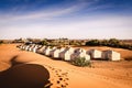 Nomad tent camp as a hotel in the middle of the desert with Moroccan building in the background.