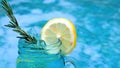 Non-alcoholic blue cocktail with rosemary and lemon slice near swimming pool