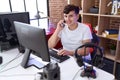 Non binary man streamer talking on smartphone using computer at gaming room