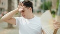 Non binary man using handfan suffering for hot at park Royalty Free Stock Photo