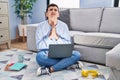 Non binary person studying using computer laptop sitting on the floor begging and praying with hands together with hope expression