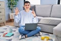 Non binary person studying using computer laptop sitting on the floor showing and pointing up with fingers number six while Royalty Free Stock Photo