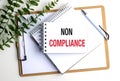 Non compliance concept shown on a notepad with office supplies and plant on white background Royalty Free Stock Photo