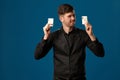 Noob in poker, in black vest and shirt. Holding two playing cards while posing against blue studio background. Gambling