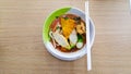 Noodle bowl that consist of fish ball, vegetable, soup and more placed on the white cup and disk on the wooden table Royalty Free Stock Photo