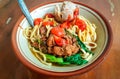 Noodle with chicken in bowl on wooden background with chicken strip, vegetable, meet ball, and chili sauce. Mie Ayam bakso