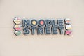 tor, canada - august 10, 2023: noodle street writing caption text illustrated animated sign on light beige wall. p