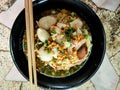 Noodles with Meatballs and pork with various seasonings placed in a black cup served with wooden chopsticks