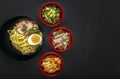 Noodles with pieces of meat and egg in a black plate and dim sum with different traditional snacks of mushrooms Royalty Free Stock Photo