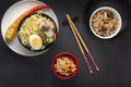 Noodles with pieces of meat and egg in a black plate and dim sums with different traditional snacks of mushrooms, Royalty Free Stock Photo