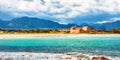 The Nora bay and beach, the medieval Sant`Efisio church near the shore and mountains in the background