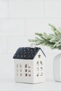 Nordic Christmas home interior decor. Small ceramic house and vase with fir branch on white table. Cozy home, hygge, Scandinavian