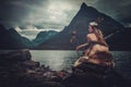 Nordic goddess in ritual garment with hawk near wild mountain lake in Innerdalen valley.