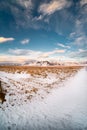 Nordic winter landscape photo. Blue sky with several clouds above snowy pasture and high mountains with sharp peaks