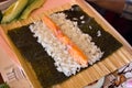 Nori algae leaf with rice and salmon fish for rolls with cucumber and avocado on a wooden board