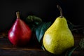 Normal view of a green or packham pear and a red or red battler pear on a table. Dark background. Organic and natural products,