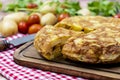 Normal view of a typical Spanish potato omelette with a separate portion with potatoes and cherrie tomatoes in a rustic setting. Royalty Free Stock Photo