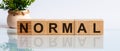 Normal is a word written in black letters on wooden cubes located on a white mirror surface. The world is changing to balance it Royalty Free Stock Photo