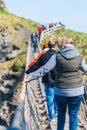 NORTHERN IRELAND, UK - 8TH APRIL 2019: Scared tourists cross the dangerous but beautiful Carrick-a-Rede Rope Bridge