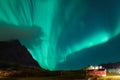 Northern lights Aurora Borealis over illuminated fishing village of reine lofoten islands. Royalty Free Stock Photo