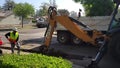 A CASE 590 Super N Backhoe Loader digs a trench with a worker in a construction vest and hardhat