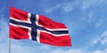 Norway flag on flagpole on blue sky background. Norwegian flag fluttering in wind against a sky with white clouds. Place for text Royalty Free Stock Photo