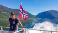 Norway - Young man taking a boat tour on the fjord. Waving Norwegian flag behind him Royalty Free Stock Photo