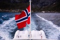 Norwegian Flag waving in the wind on a boat with landscape with Reine fjord, Lofoten Islands, mountains and glacier in Norway Royalty Free Stock Photo
