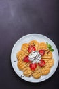 Norwegian heart shaped waffles topped with strawberries, mint and whipped cream on white plate and black background. Royalty Free Stock Photo