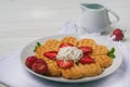 Norwegian heart shaped waffles topped with strawberries, mint and whipped cream on white plate and white wooden background. Royalty Free Stock Photo