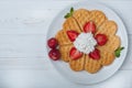 Norwegian heart shaped waffles topped with strawberries, mint and whipped cream on white plate and white wooden background. Royalty Free Stock Photo