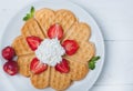 Norwegian heart shaped waffles topped with strawberries, mint and whipped cream on white plate and white wooden background. Royalty Free Stock Photo