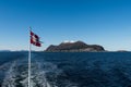 Norwegian mail or post flag hoisted on post of mailboat waving in the wind with open sea and mountains on sunny winter day Royalty Free Stock Photo