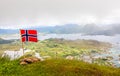 Norwegian national flag in the wind on the top of Nonstinden peak with fjord in the background, Ballstad, Vestvagoy Municipality,