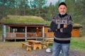 A Norwegian with a typical sweater stands in front of a small wooden house with a grass roof. Royalty Free Stock Photo