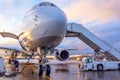 Nose view of an airplane with gangway for boarding parked at an airport during sunset bright light shine and clouds in the sky