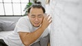 Nosy young chinese man sneakily listening through bedroom wall with glass, overcome by curiosity and eavesdropping in a secret